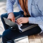 Homme prenant des notes dans un classeur sur un banc avec un café à proximité