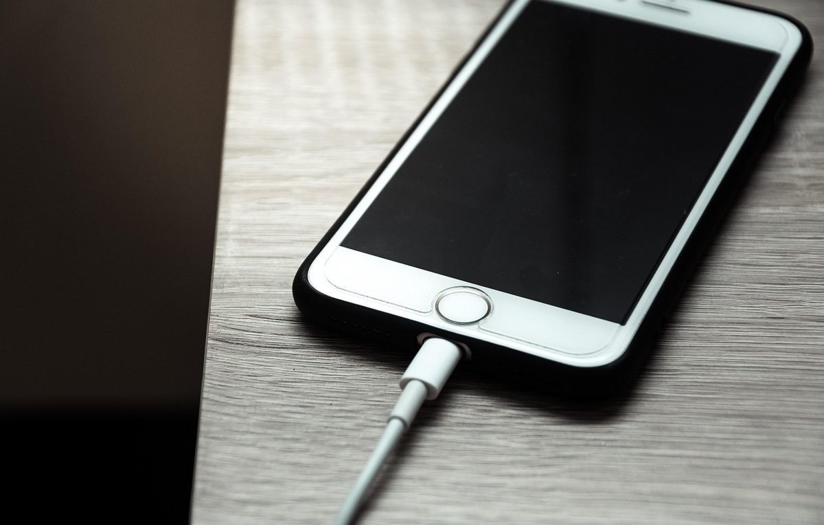 Un téléphone iPhone blanc connecté à un câble de recharge sur une surface grise