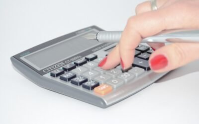 Une main aux ongles rouges appuie sur une calculatrice avec un stylo